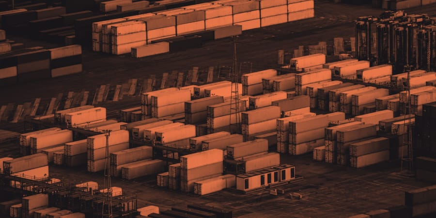 Stacks of standard shipping containers at a port, one format moving between ship, rail, and road